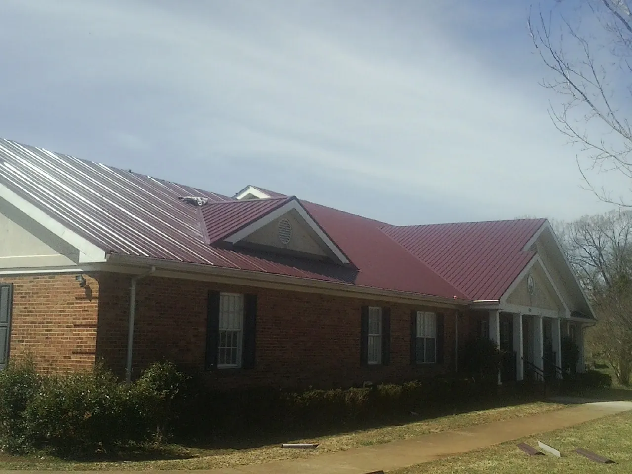 Red metal roof with gabled entries on a long brick building, from a Hail Damage Roof Repair job in Winsted