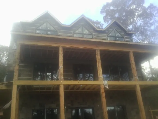 Dormers and porch framing on a large log home under construction — Roof Coating work by our crew in Winsted