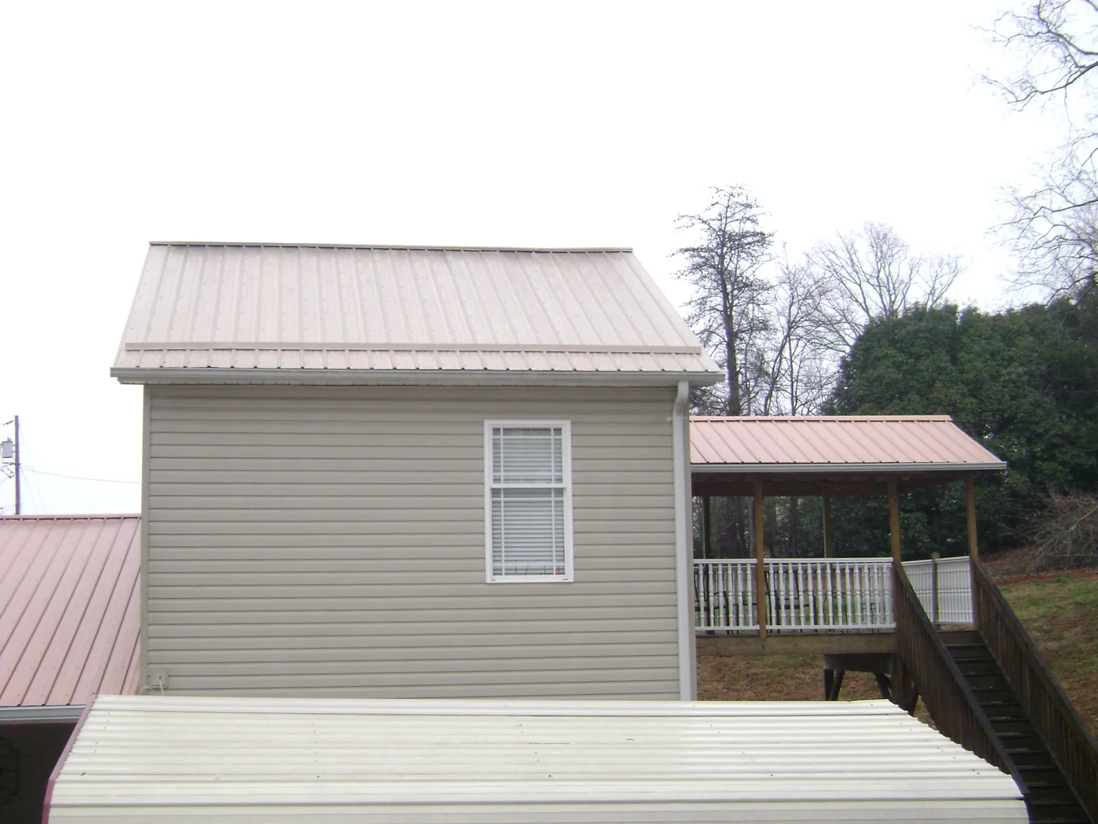Tan metal roofs on a two story addition and attached porch, from a Roof Replacement job in Winsted