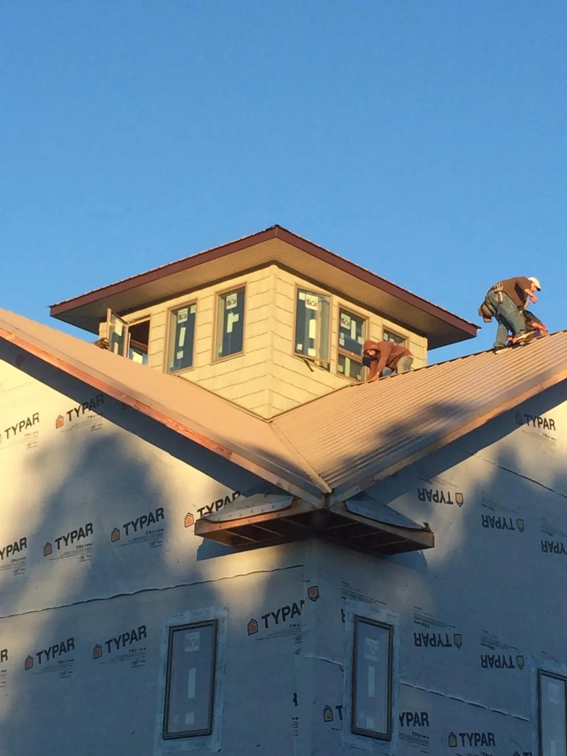 Roofers working around a rooftop cupola on a new metal roof at sunset — Roof Waterproofing in Winsted by Roofing Brothers
